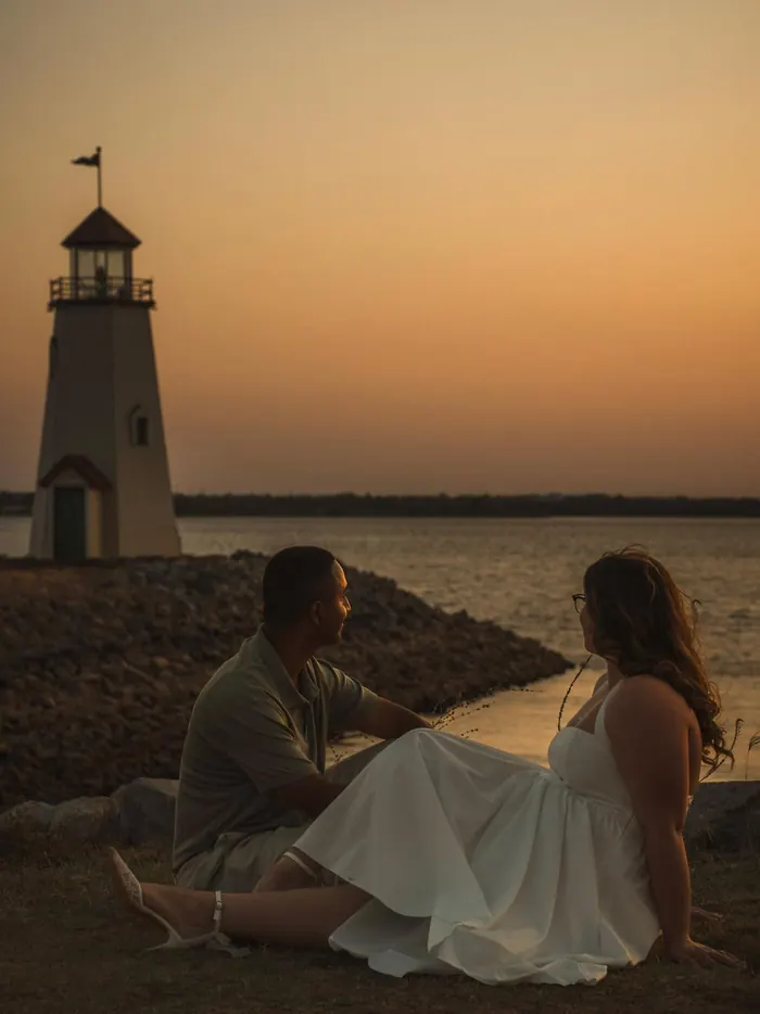 Couple sitting on the rocks by a lighthouse at sunset