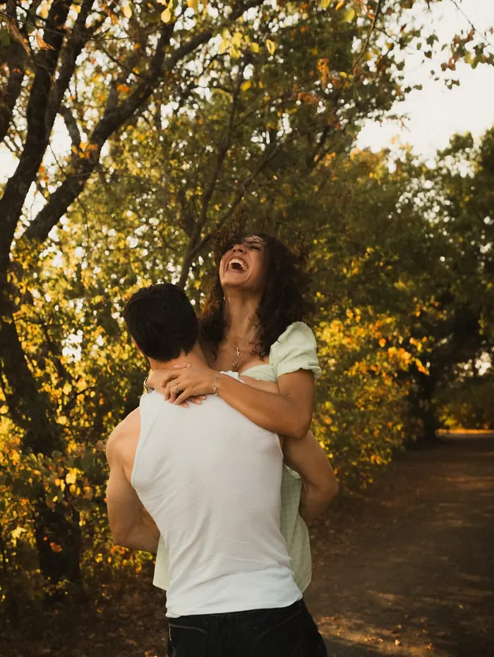 Man lifting his laughing girlfriend in a sunlit grove