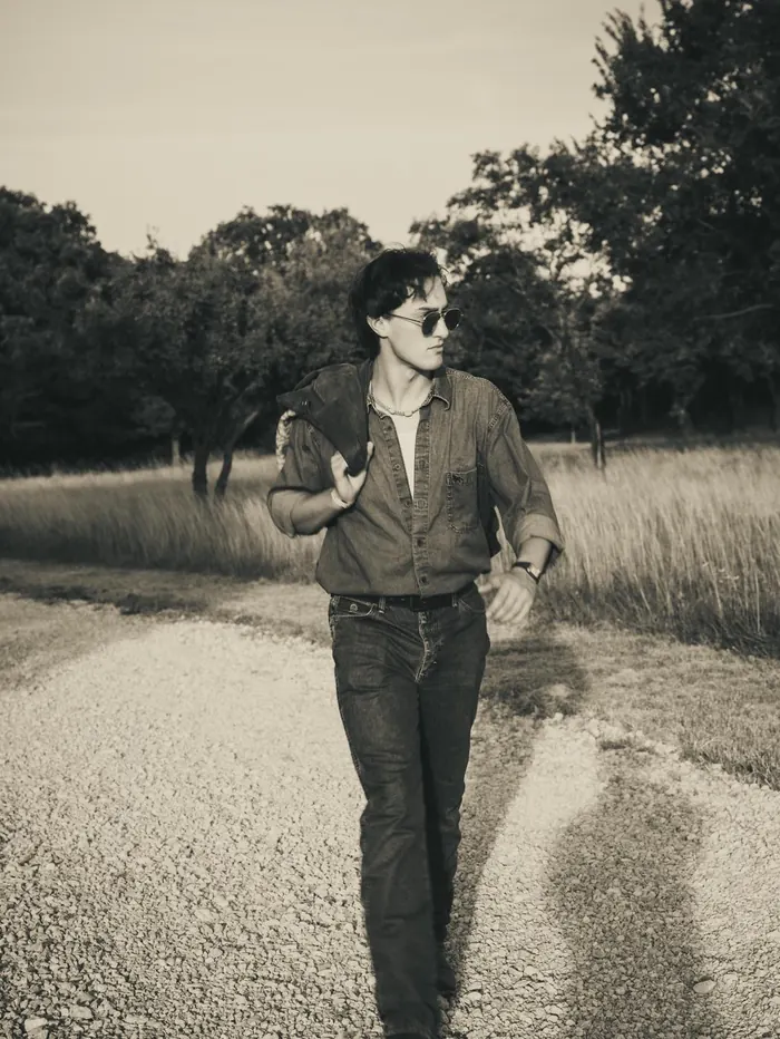 Black and white portrait of a young man walking down a gravel road