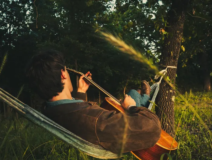Young man playing guitar in a hammock under the trees