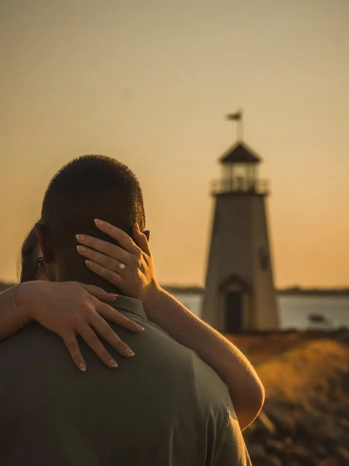 Couple embracing in front of a lighthouse at golden hour