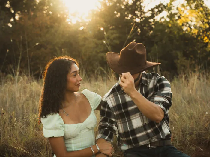 Couple laughing together in tall grass at sunset