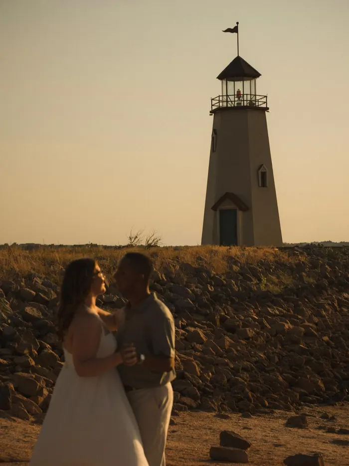 Couple standing close in front of a lighthouse at dusk