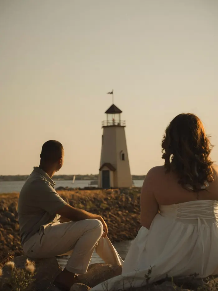 Couple sitting together facing a lighthouse at sunset