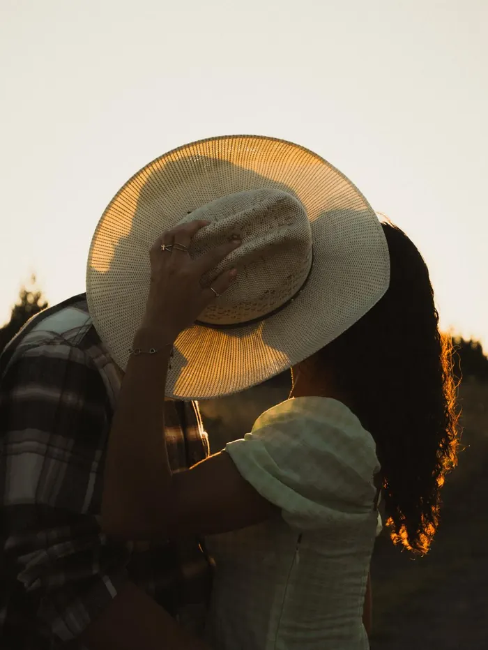 Couple kissing behind a straw sun hat at golden hour