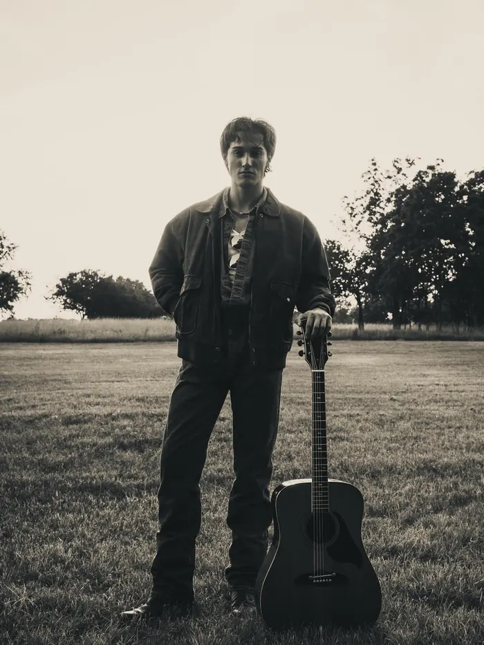 Black and white senior portrait of a young man with his guitar