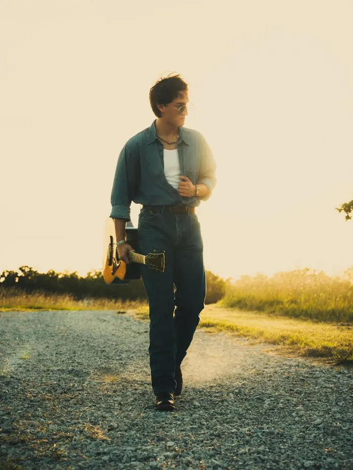 Senior walking down a country path carrying a guitar