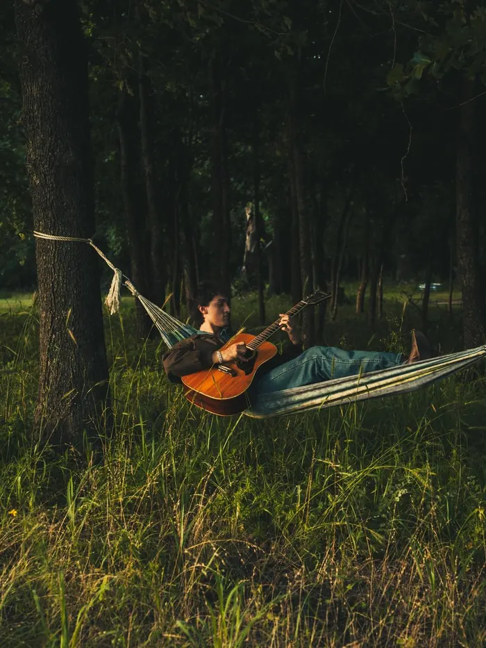 Young man relaxing in a hammock with his guitar in the woods