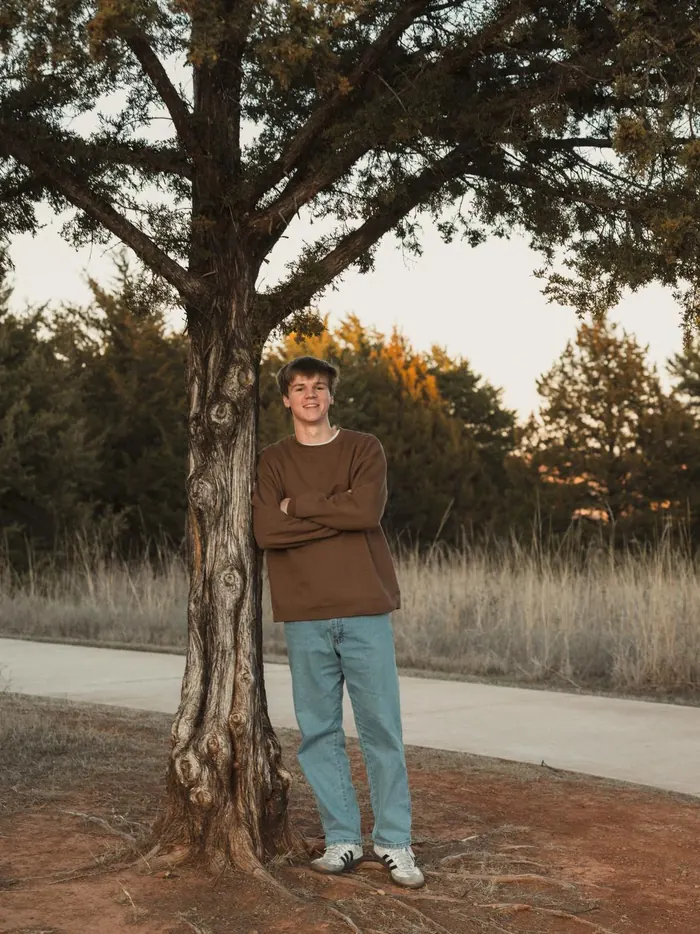 Senior leaning against a tree beside a path